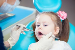 A young toddler girl with pigtails and pink bows that is having her teeth examined at a dental office. 