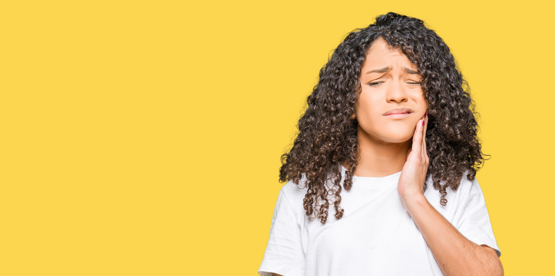 Young woman holding jaw in pain on a yellow background