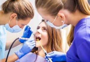 Two female dental assistants examining and cleaning a young woman's teeth. 