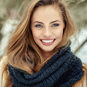 A beautiful blonde-brown woman that is smiling at the camera outside in the winter. She has a beautiful smile.