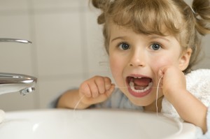 Young female child looking at the camera and flossing her teeth.