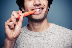Close-up view of a male eating a carrot and smiling.