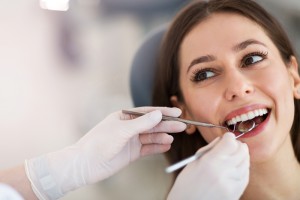 A young adult brunette woman that is having her teeth checked at a dental office. Only the woman's face and the dental hygienist's hands with dental tools are showing.