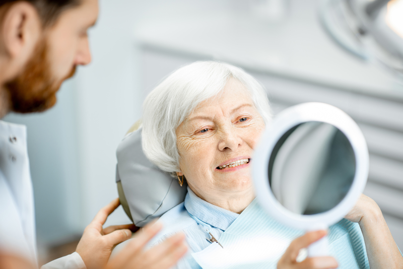 Elderly woman at the dentist smiling into a hand-held mirror