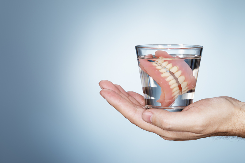 Man holding a glass of water with dentures in it.