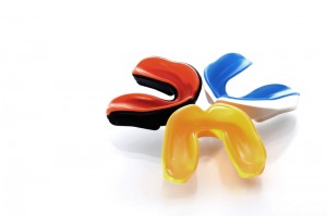 Three mouth guards together on a white backdrop. There is a red and black one, a blue and white one and a yellow one. 