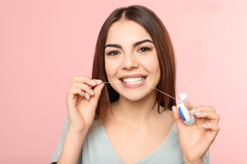Young woman flossing teeth standing in front of a pink background.
