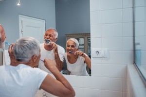 Senior citizen couple that is brushing their teeth in a mirror together.