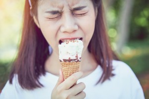 Girl that has sensitive teeth while she is biting into an ice cream.