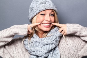 cheerful young sophisticated blond woman playing with a fake smile for a sexy warm winter, grey background