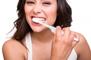 Brunette woman that is smiling and brushing her teeth with excitement.