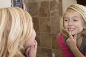 Child looking in mirror and pointing at missing front tooth