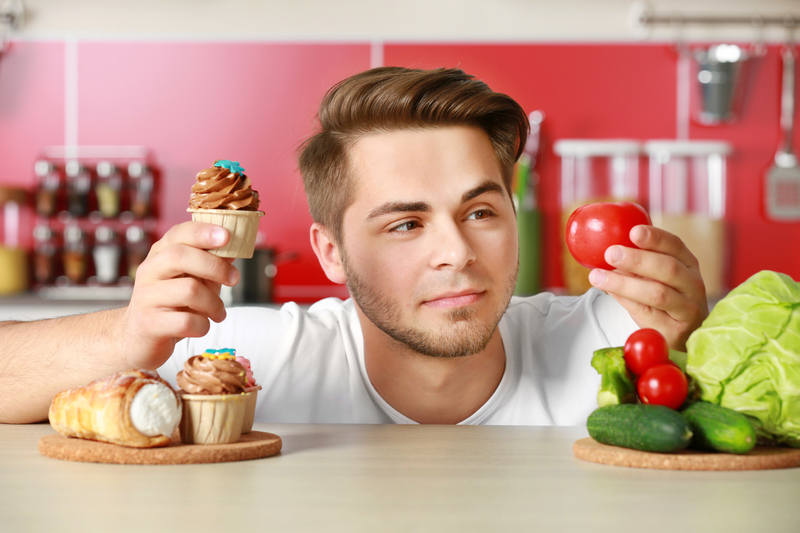 man holding a cupcake in one hand and a tomato in the other with a questionable look on his face.